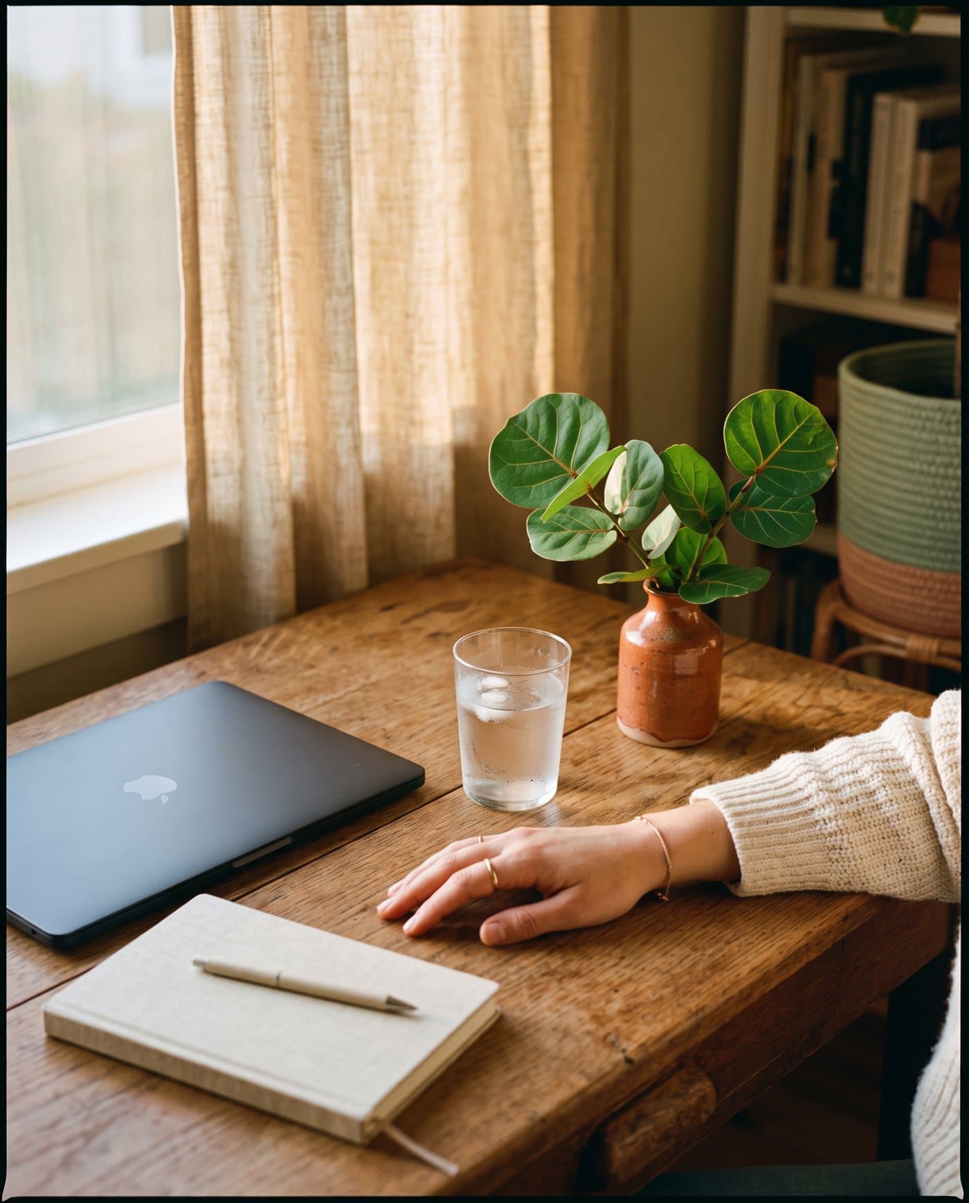 A closed laptop and notebook set aside on a wooden desk in soft afternoon light